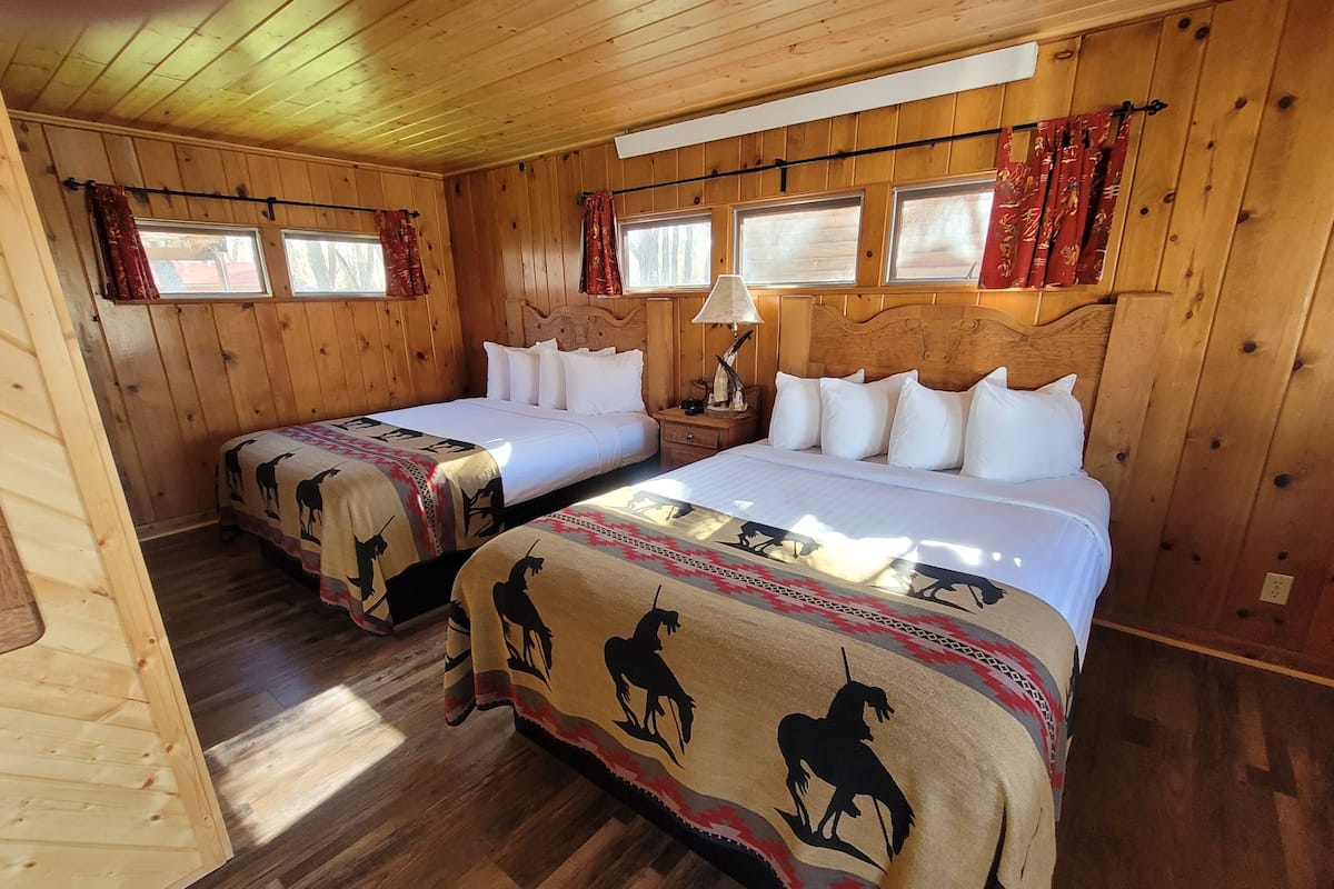 A room with two beds, wooden walls, and a wooden floor.