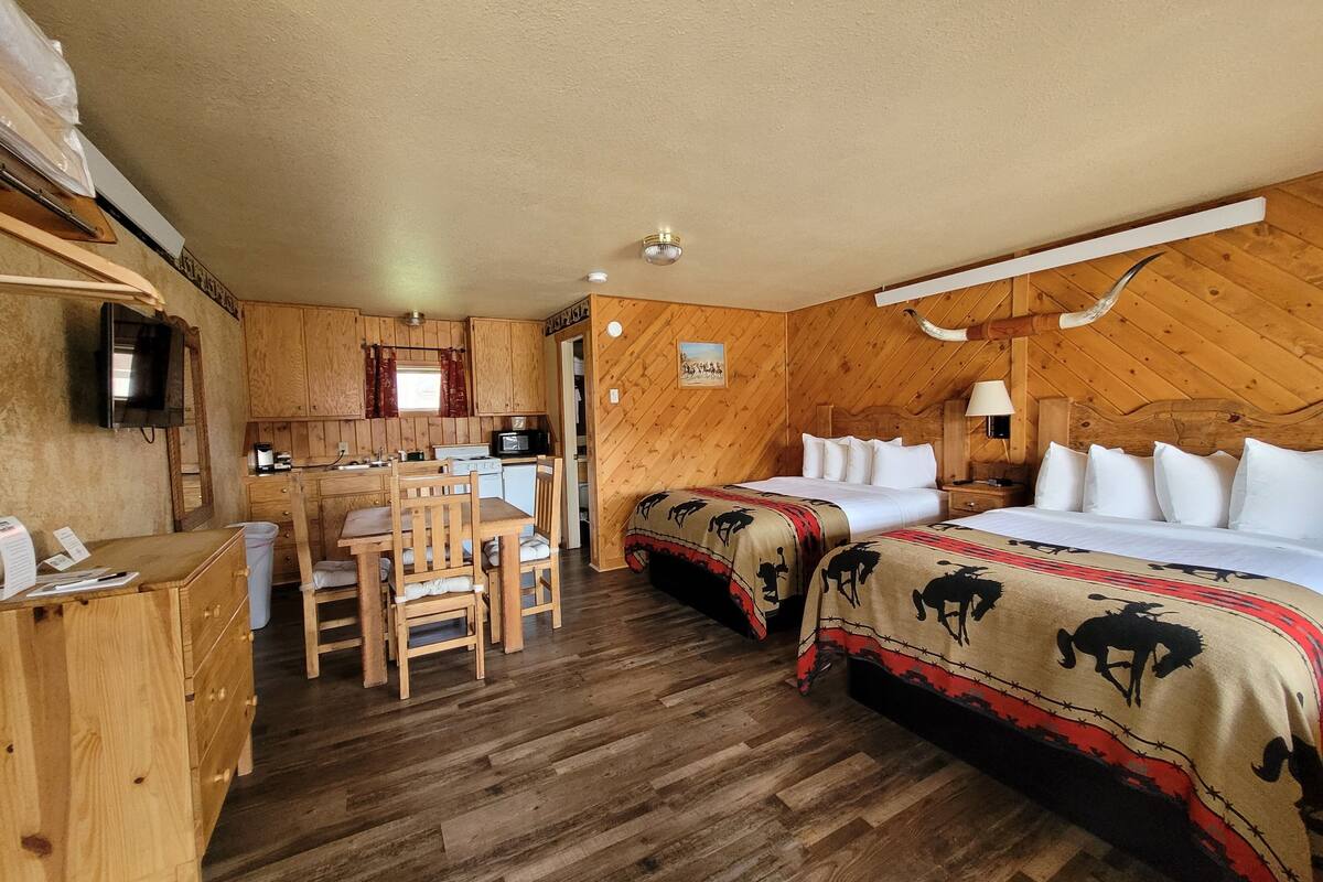 A wooden interior with a kitchen, two beds with patterned blankets, a desk, and a television.