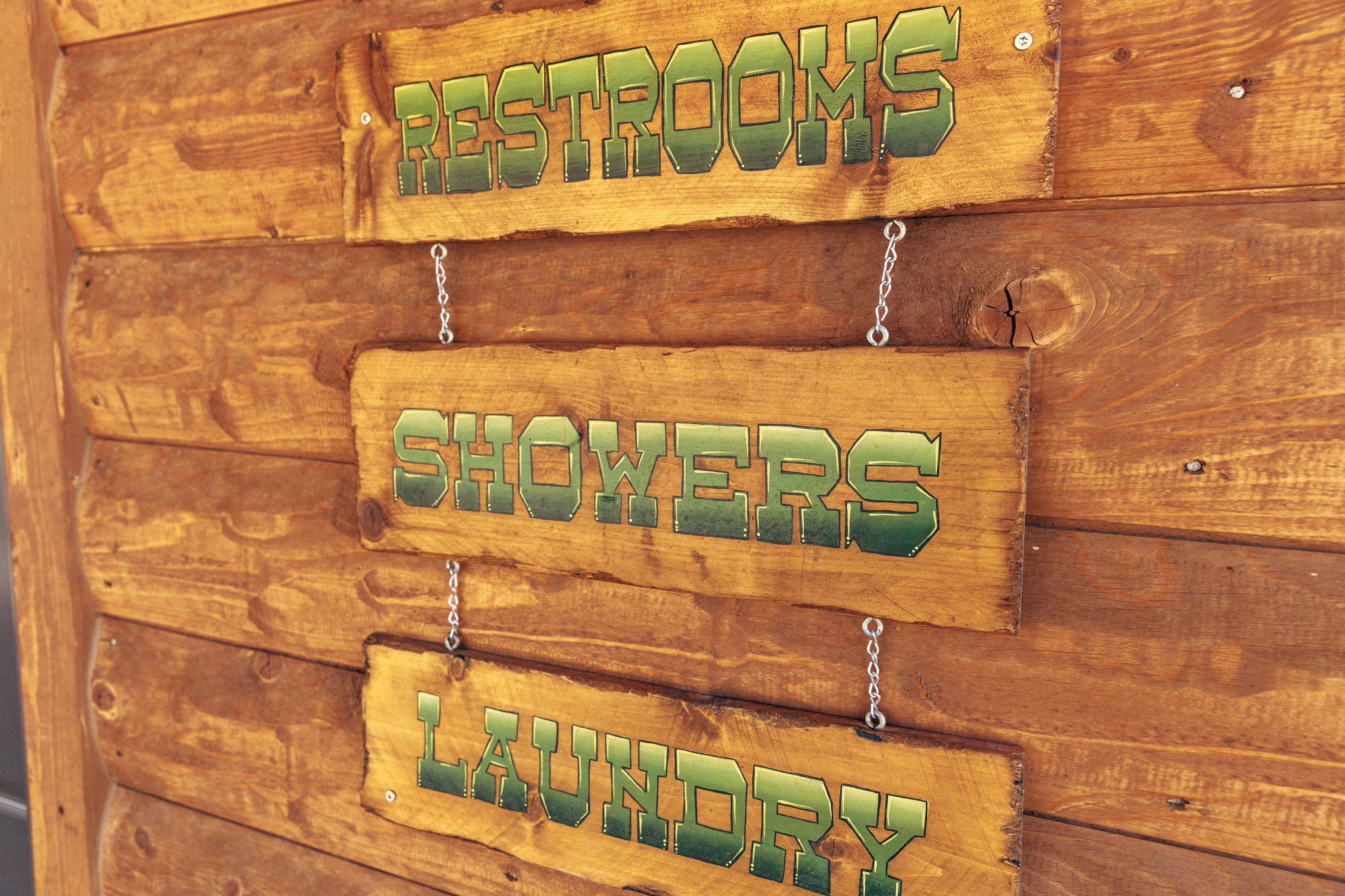 Un letrero de madera con tres secciones que indican: baños, duchas y lavandería.