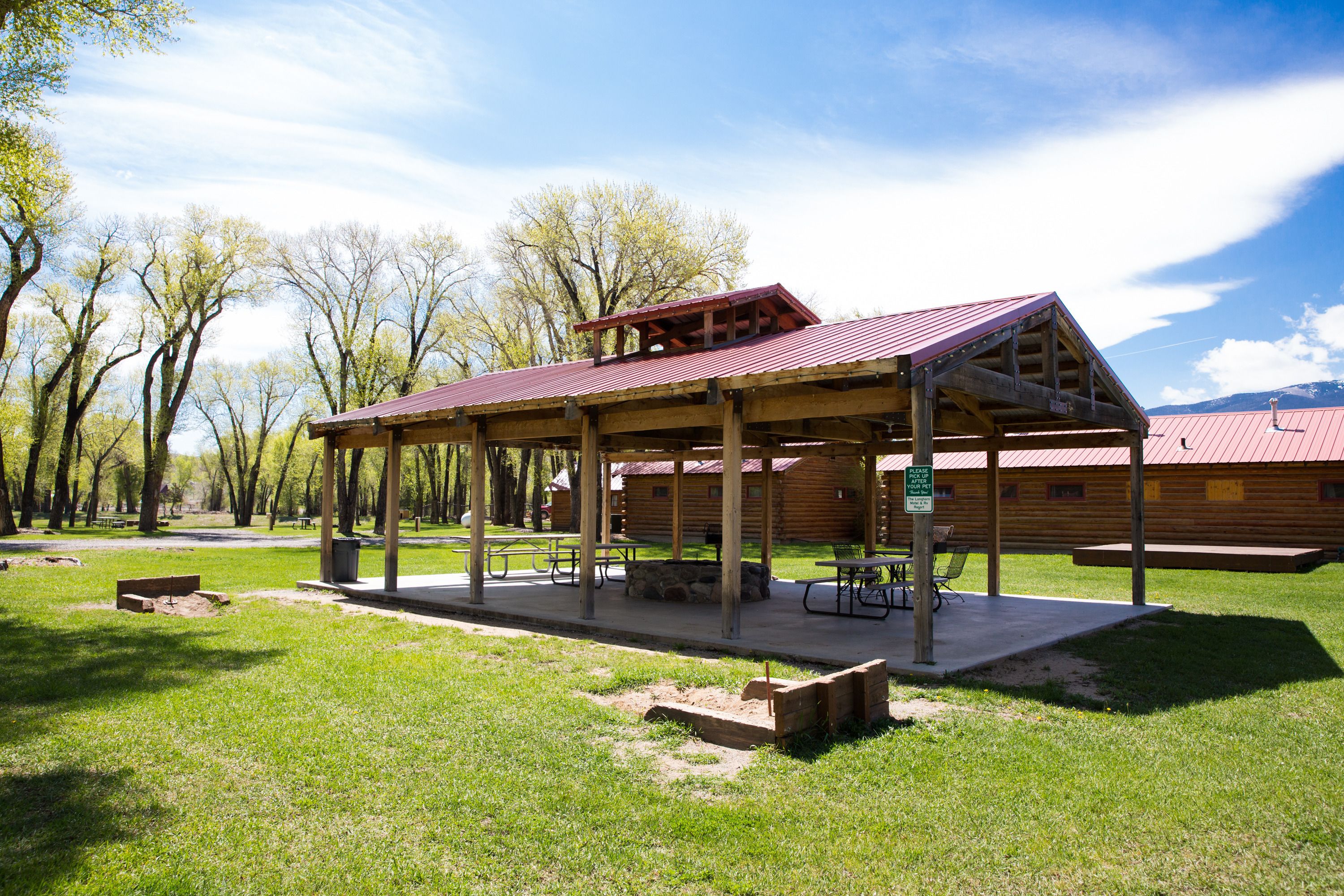 Una cabaña de madera con porche cubierto, mesas de picnic y un banco.
