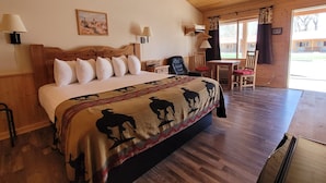 Un dormitorio con una cama grande, cabecera de madera y una manta con siluetas de caballos. Hay dos mesitas de noche con lámparas, una silla y un escritorio con silla.