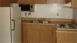A compact kitchen with wooden cabinets, a microwave, a sink, and a stove. - Colonade Motel (Mesa)