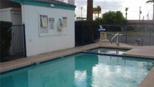 A swimming pool with a tiled deck and a small building with a sign. - Colonade Motel (Mesa)