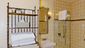 A bathroom with a glass-enclosed shower, a white sink, and a bamboo shelf with towels.