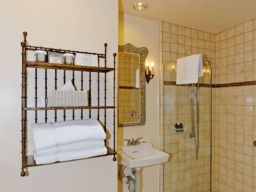 A bathroom with a glass-enclosed shower, a white sink, and a bamboo shelf with towels.