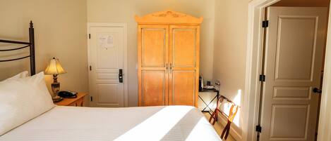 A hotel room with a bed, a nightstand, a lamp, a wardrobe, and a door.