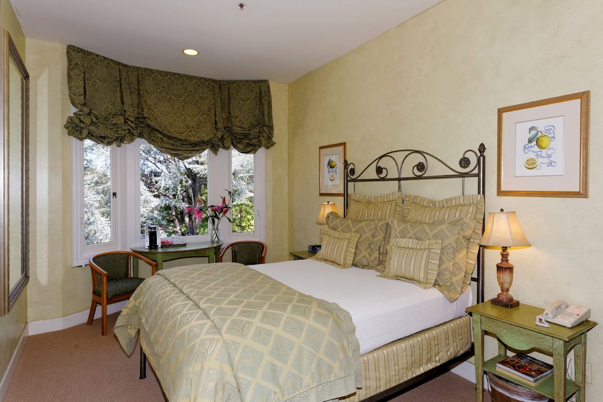 A bedroom with a bed, a nightstand with a lamp, a chair, and a window with curtains.