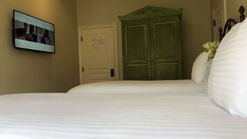 Una habitación de hotel con una cama, un armario verde, una puerta con un aviso y un televisor mostrando una escena.