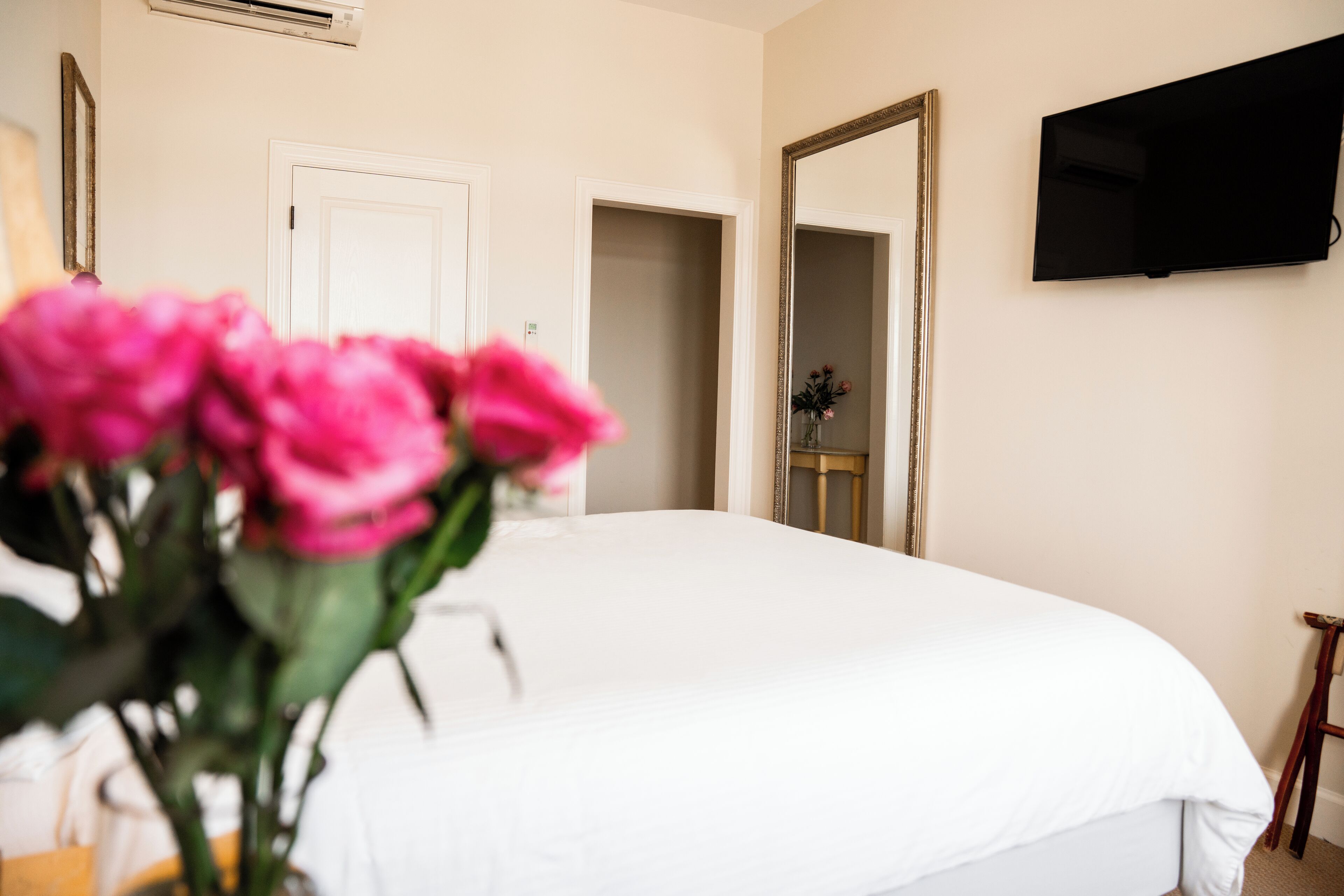 A bedroom with a large bed, a TV mounted on the wall, and a door leading to another room.