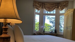 Un dormitorio con una cama grande, una lámpara, una ventana con cortinas, un escritorio con silla y un armario.