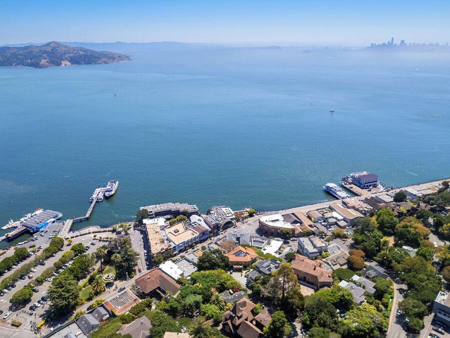 An aerial view of a coastal city with a marina, buildings, and a distant mountain range.