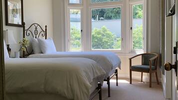 Um quarto com uma cama grande, uma cadeira, uma janela com cortinas e um quadro na parede.