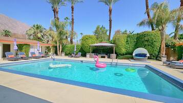 A swimming pool with lounge chairs and umbrellas, surrounded by palm trees and greenery.