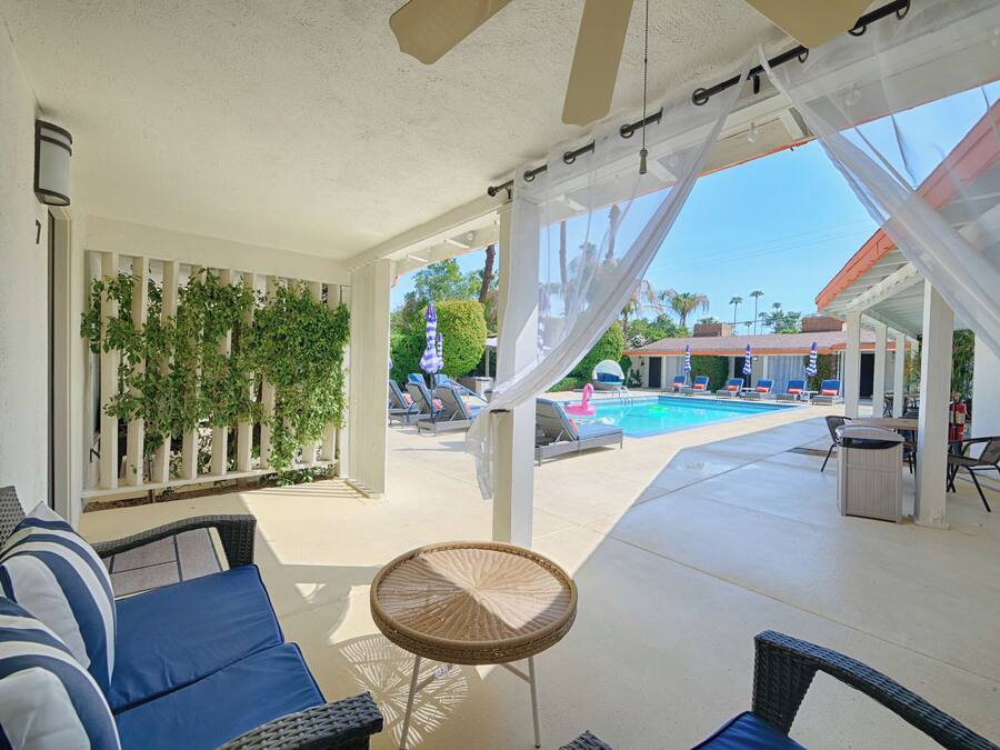 A covered outdoor area with a pool, lounge chairs, and a seating area with cushions and a small table.