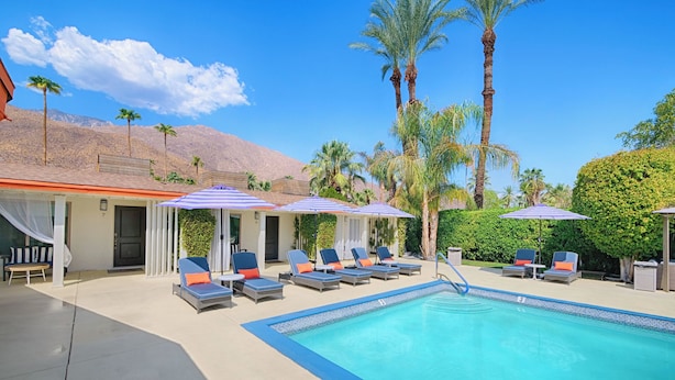 A pool area with lounge chairs and umbrellas, surrounded by palm trees and a mountain in the background. - Little Paradise Hotel (Palm Springs)