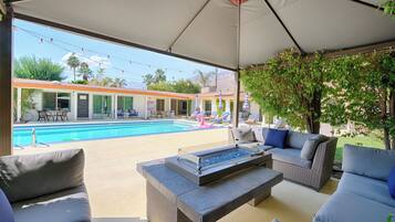 A covered outdoor area with a pool, lounge chairs, and a fire pit.
