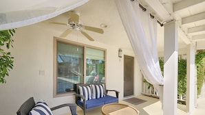 A covered outdoor seating area with wicker furniture and a ceiling fan. - Little Paradise Hotel (Palm Springs)