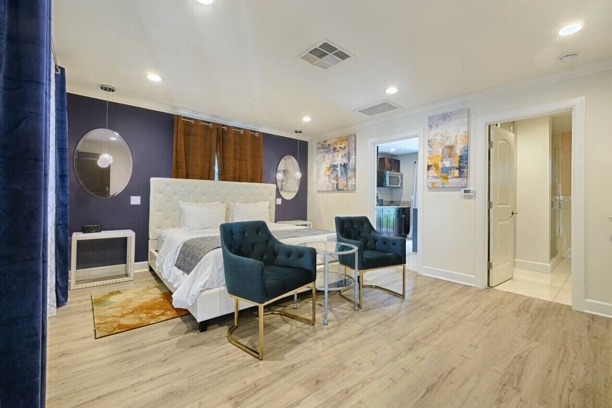 A modern bedroom with a bed, two armchairs, a small table, and a mirror.