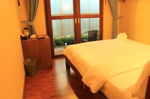 A bedroom with a bed, a desk, a chair, and a view through a glass door to an outdoor area.