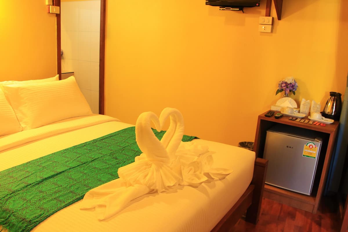 A hotel room with a bed, a green throw blanket, a refrigerator, and a small table with a vase of flowers.