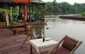 A wooden deck with a table and chairs overlooking a calm river. - Pongsuda Chalet (Sai Yok)
