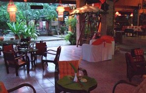 An indoor dining area with tables and chairs, some covered with tablecloths, and hanging lanterns.