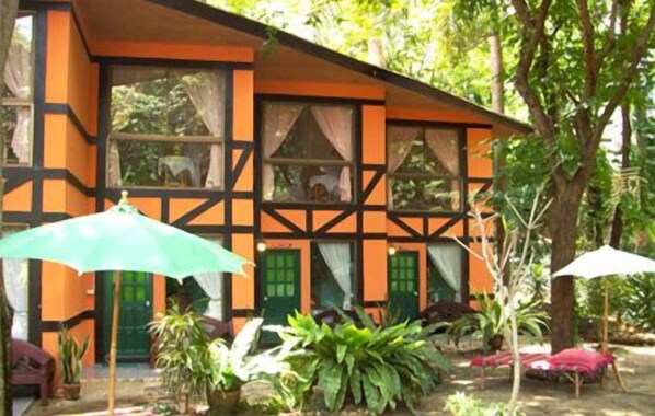 A building with a distinctive architectural style featuring a combination of orange and black colors, large windows, and a garden area with potted plants and umbrellas.