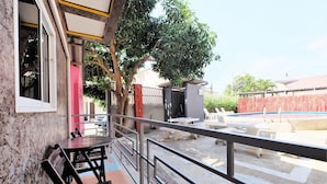 Un balcón con mobiliario exterior, barandilla metálica y vista a una piscina.