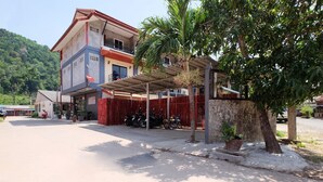 Un edificio de varios pisos con un área de estacionamiento techada, una cerca roja y una palmera.