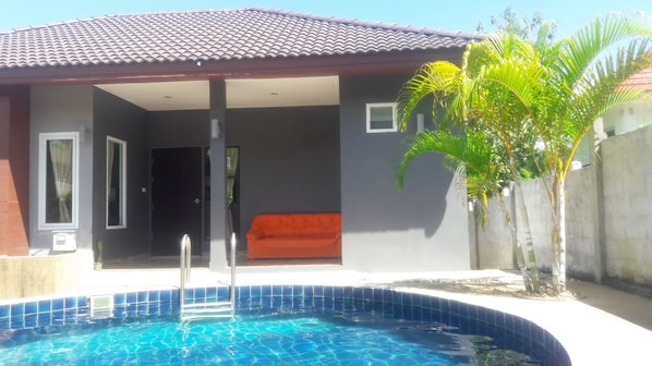 Una casa moderna con piscina, un patio cubierto y una palmera.