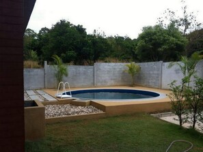 Una piscina rectangular con escalera, rodeada por un patio de concreto y una zona de césped.