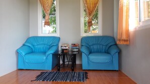 A room with two blue armchairs, a small table with books, and a patterned rug on a wooden floor. - Lanta Dream Garden Pool Villa (Ko Lanta)