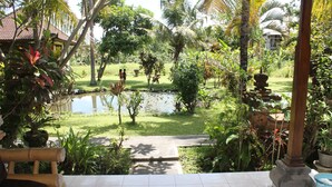 A garden with a pond, a wooden bench, and a tiled patio area. - Swan Inn (Ubud)