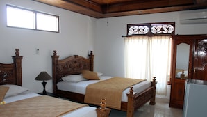 A hotel room with two wooden beds, a wooden wardrobe, a refrigerator, and a window with curtains. - Swan Inn (Ubud)