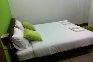 A neatly made bed with white linens and green pillows, a bedside table, and a green rug. - Lanta Sun Smile Place (Ko Lanta)