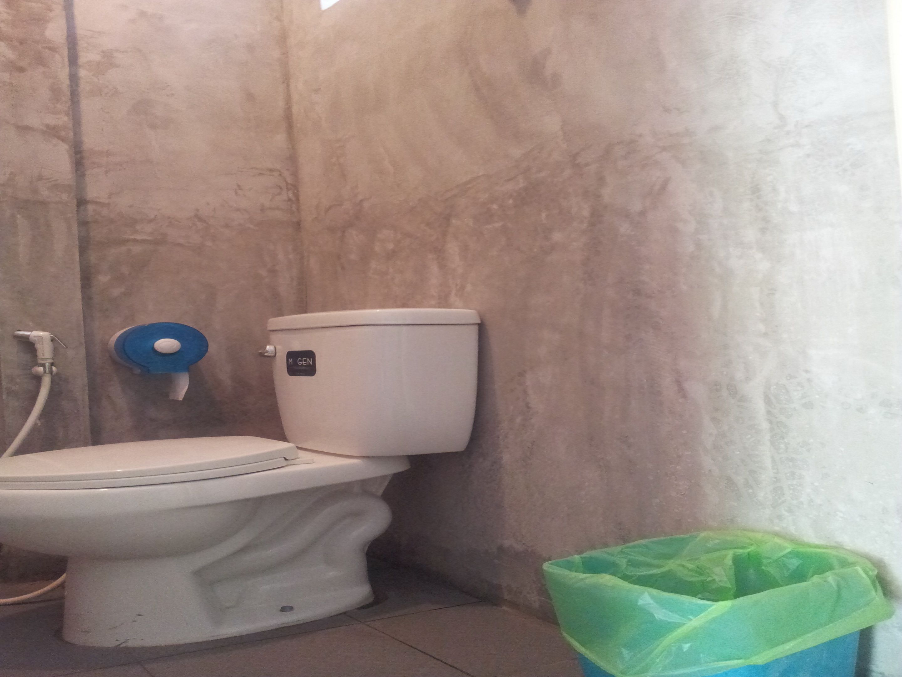 A bathroom with a toilet, a wall-mounted bidet, and a green trash bin.