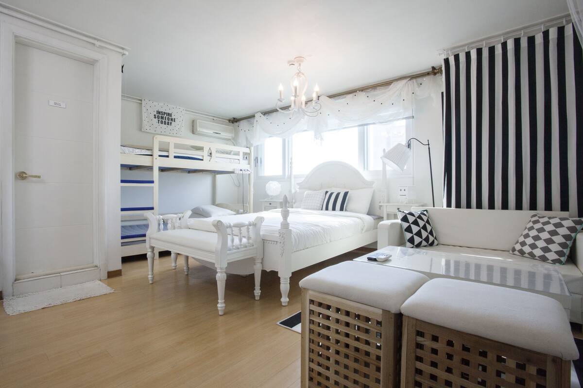 A bedroom with a bunk bed, a sofa, a bedside table, and a chandelier.