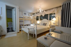 A bedroom with a bunk bed, a bedside table with a lamp, a chair, and a small table with a remote control.