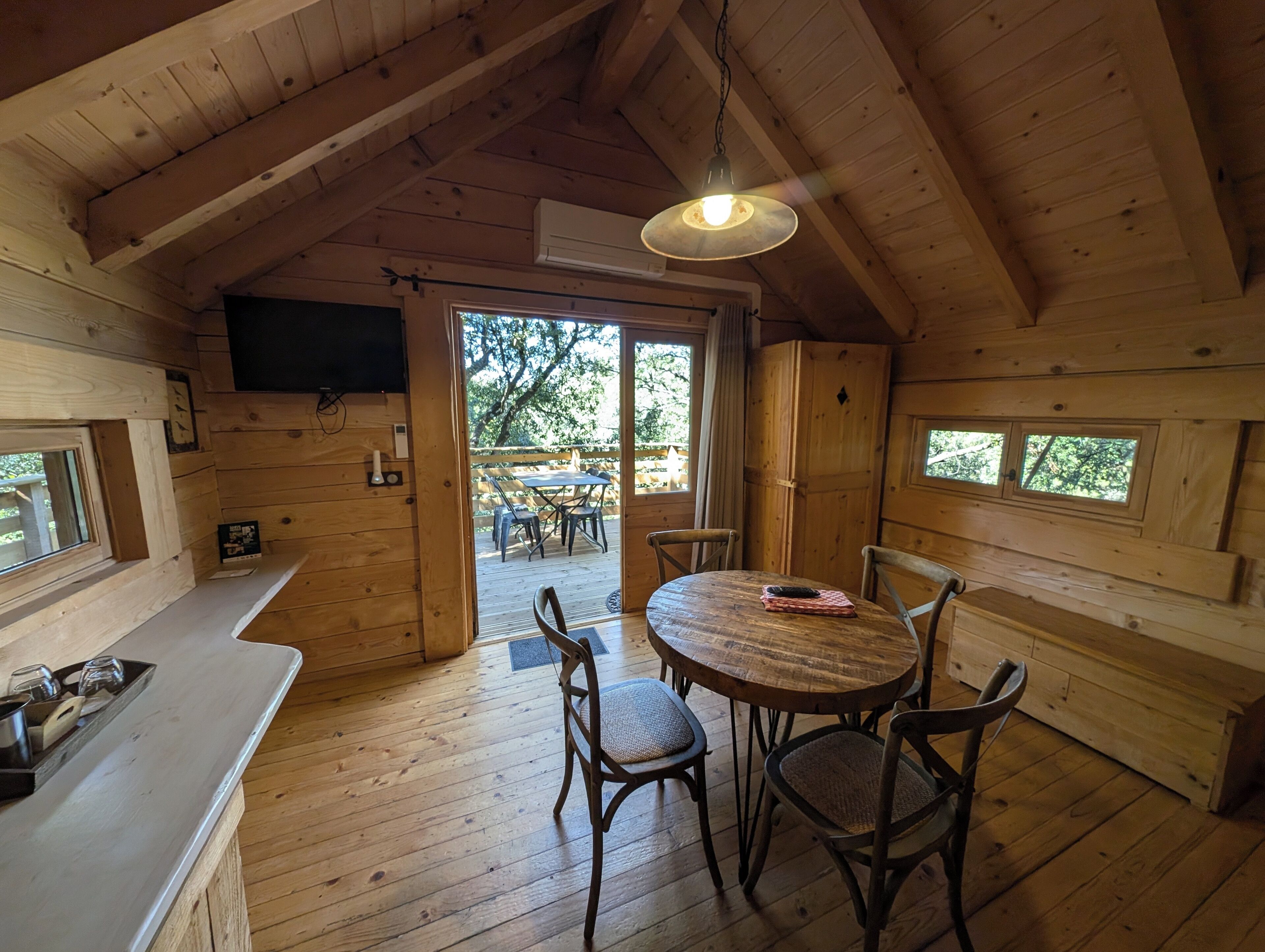 A wooden cabin interior with a dining area, a kitchen counter, and a television mounted on the wall.