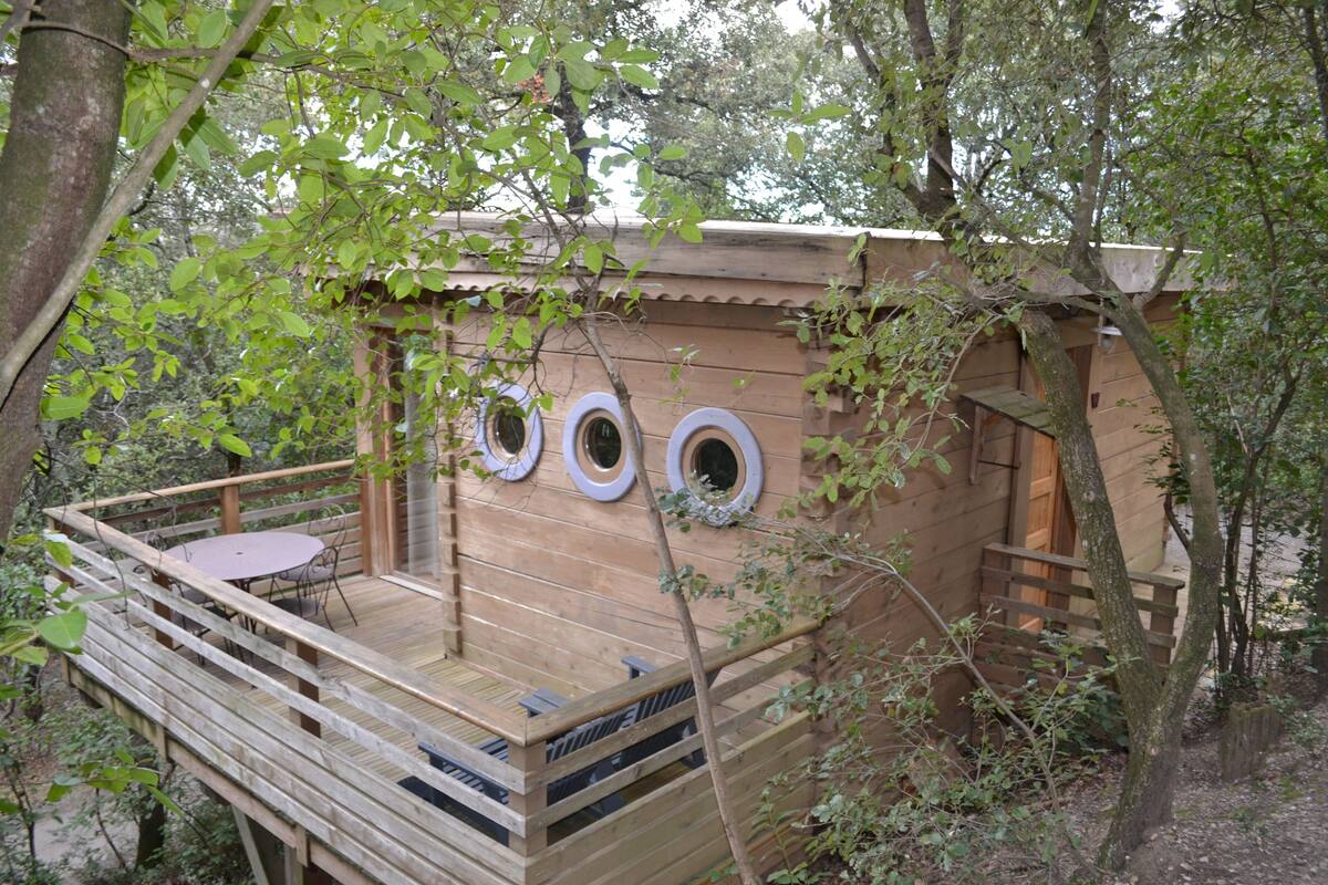 Eine Holzhütte mit einer Veranda, einem runden Tisch und drei Rundfenstern.