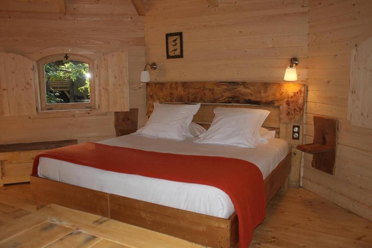Ein Schlafzimmer einer Holzhütte mit einem Bett, einem Fenster und Wandlampen.
