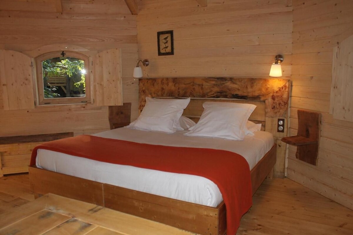 A wooden cabin bedroom with a bed, a window, and wall-mounted lamps.