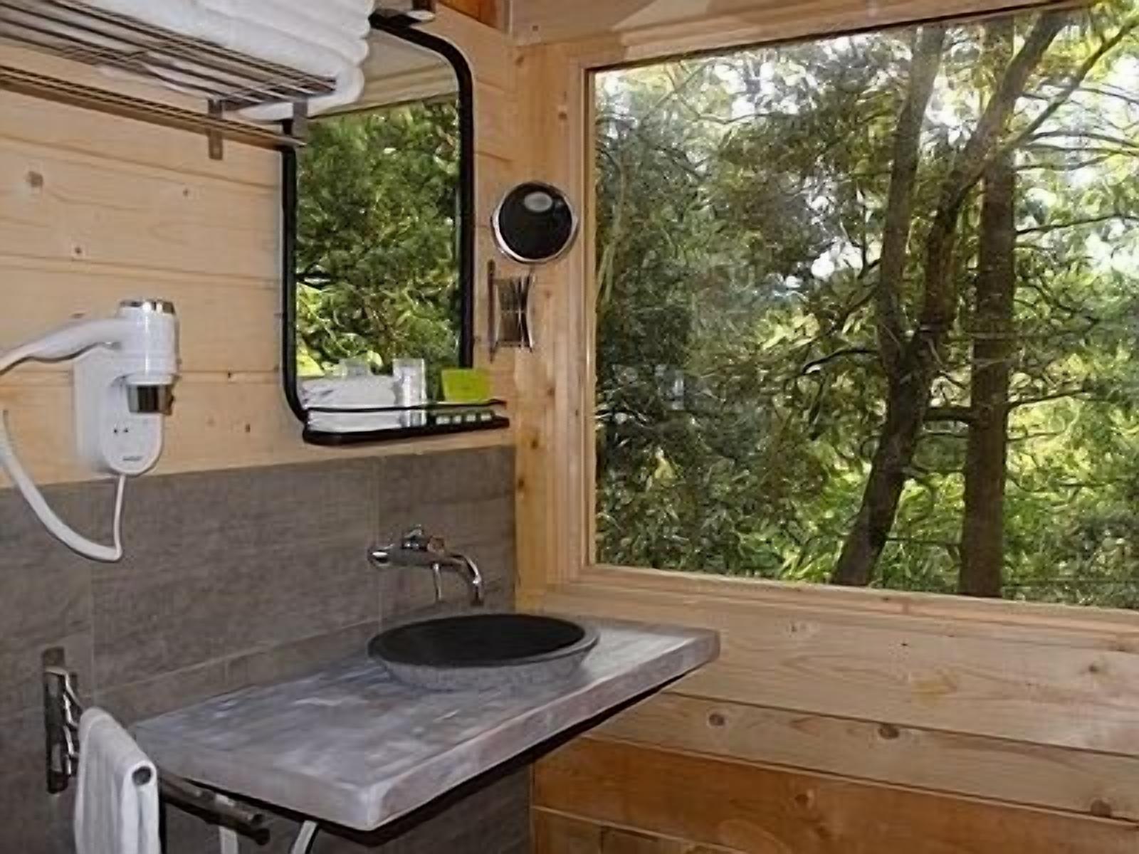 Un baño con detalles de madera, un lavabo, un espejo y una ventana con vistas a árboles.