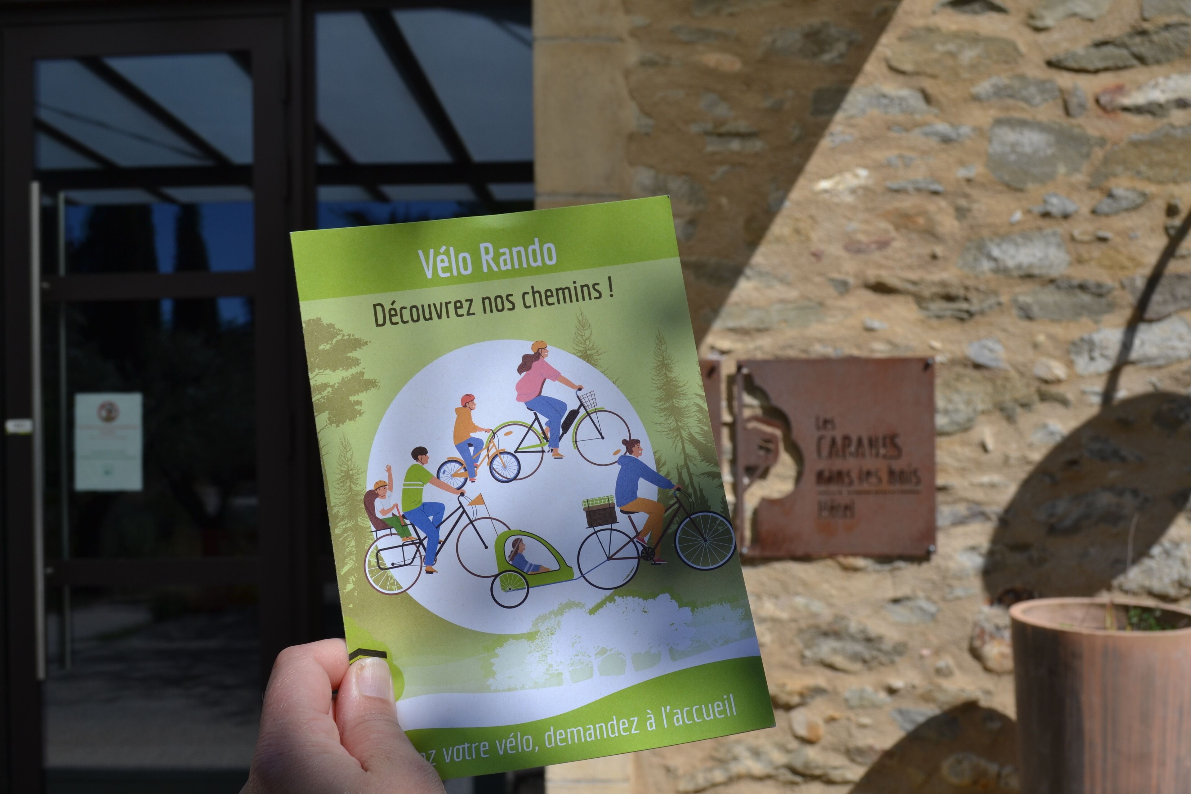 A hand holding a brochure titled "Vélo Rando" with illustrations of cyclists.