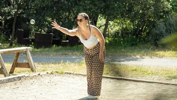 A person in a white tank top and patterned pants standing on a concrete path with a wooden structure in the background.