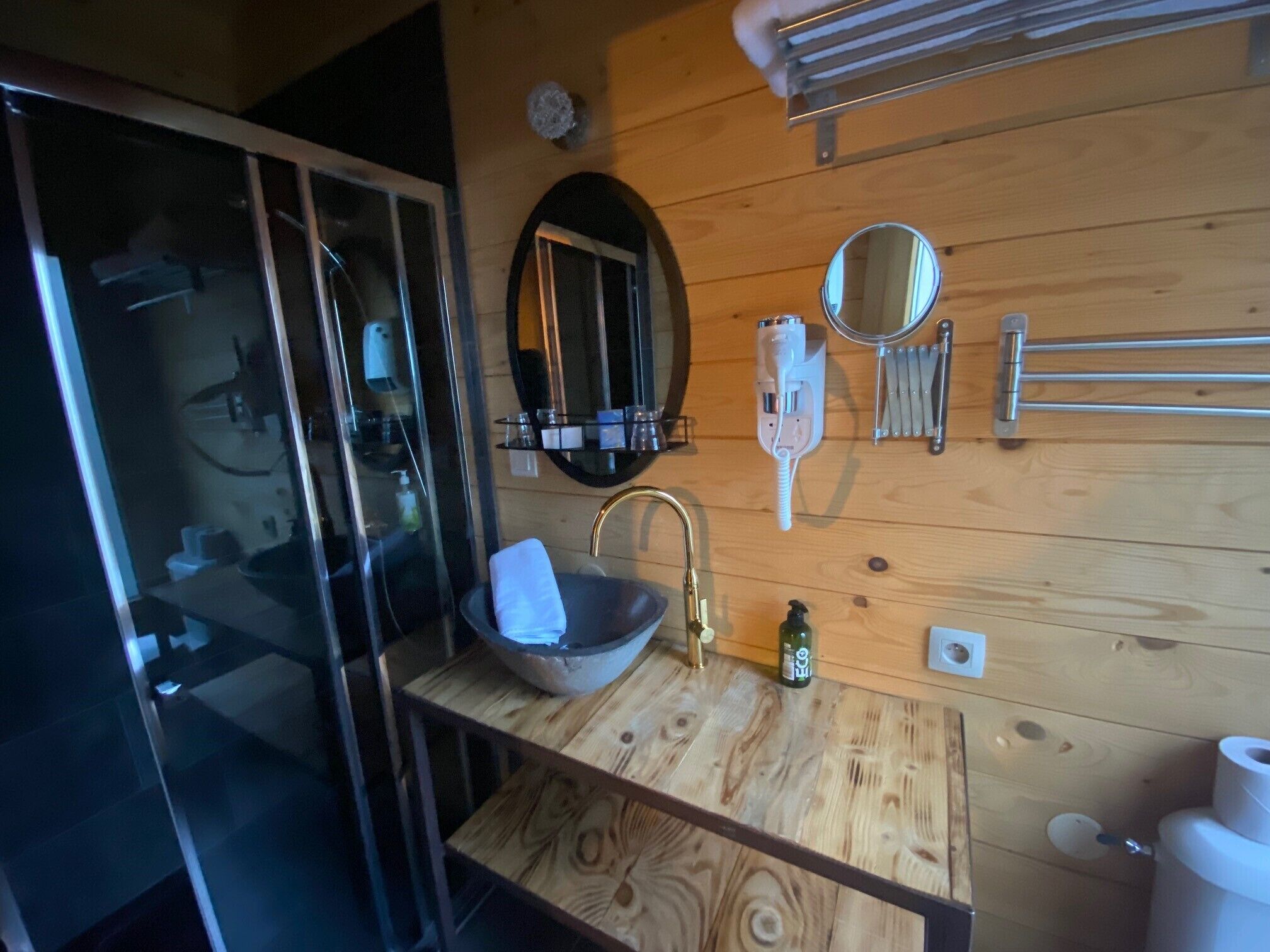 A bathroom with a wooden vanity, a sink with a gold faucet, a mirror, and a towel rack.