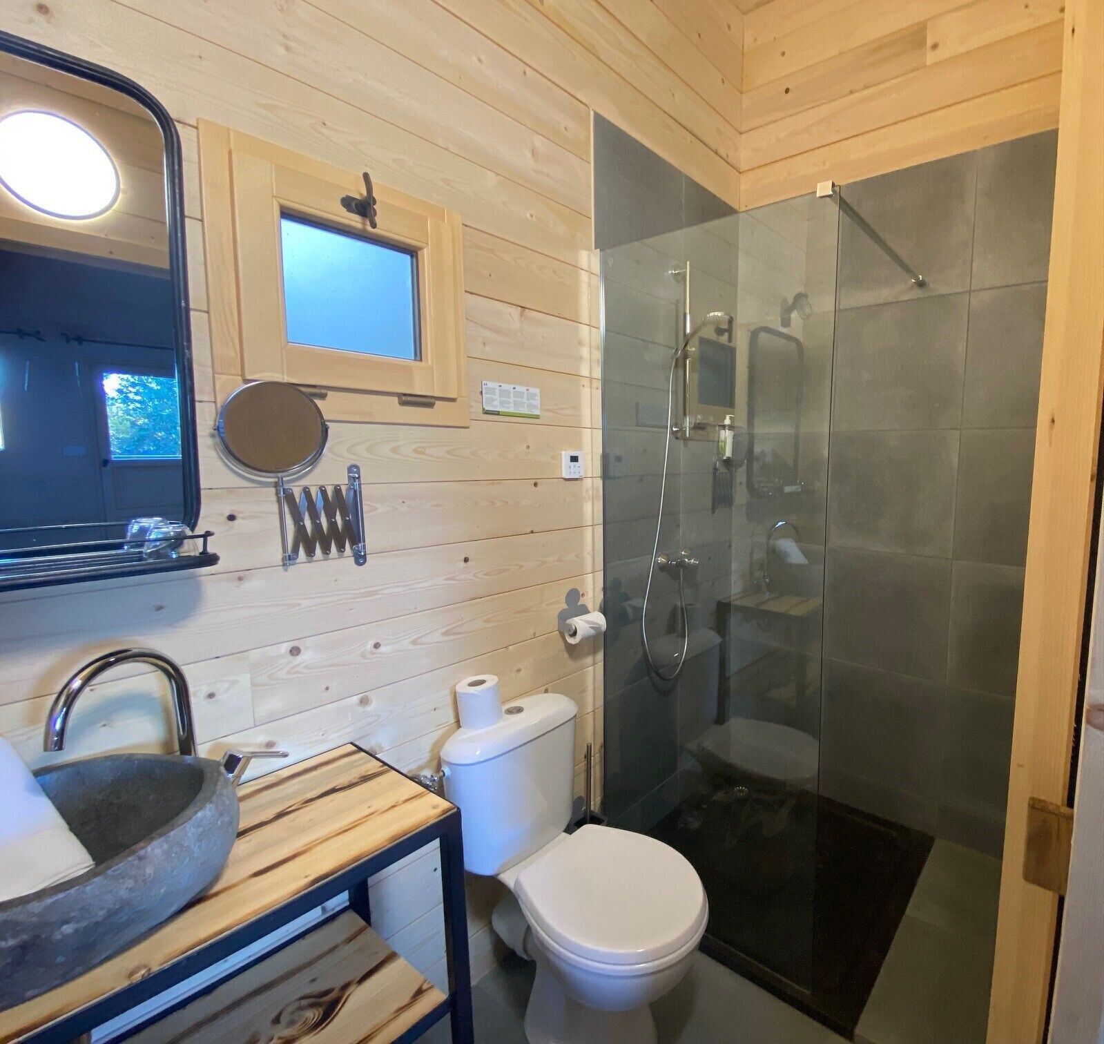 Un baño pequeño de madera con cabina de ducha de vidrio, lavabo y retrete.