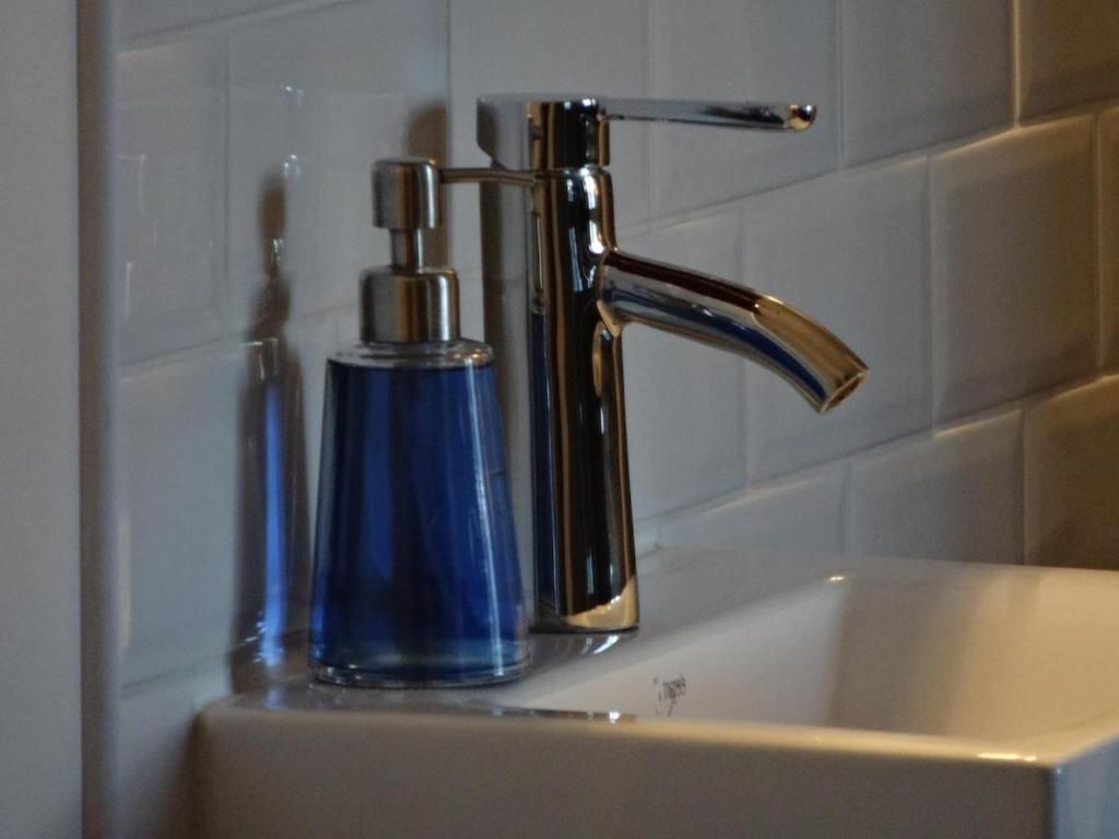 Un grifo cromado y una botella azul sobre un lavabo blanco.