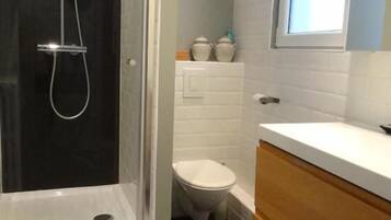 A bathroom with a glass-enclosed shower, a white toilet, and a wooden vanity.