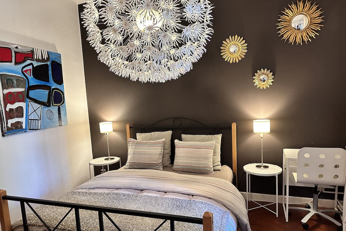 Un dormitorio con una cama, dos mesitas de noche, una silla y decoración mural.